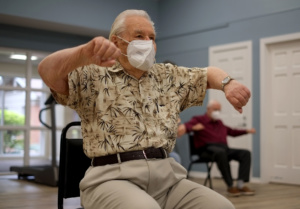 a senior male does chair exercises while wearing a face mask